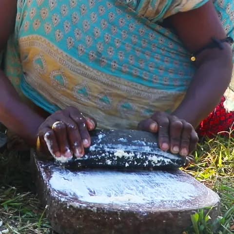 Hands grinding the soaked dal into a white paste on a sheel-nora, the traditional grinding stone