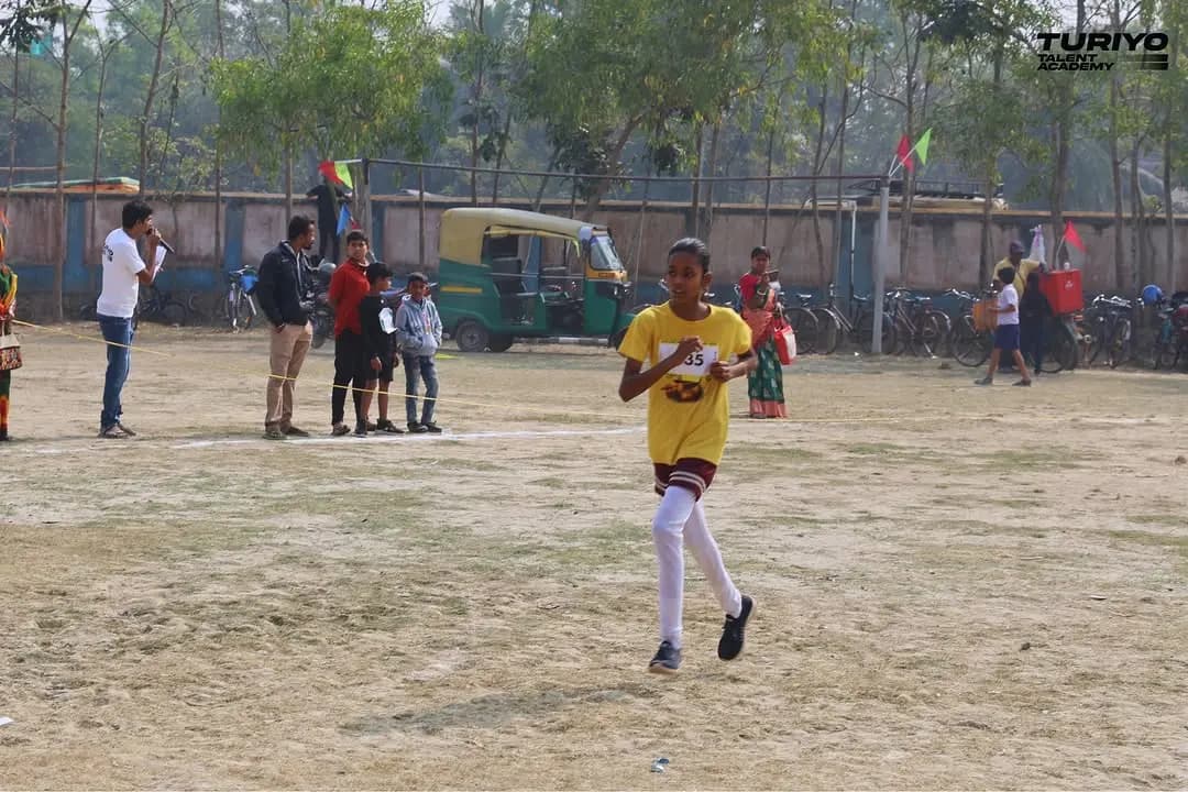 A girl in a yellow shirt and race bib runs across the field towards the finish