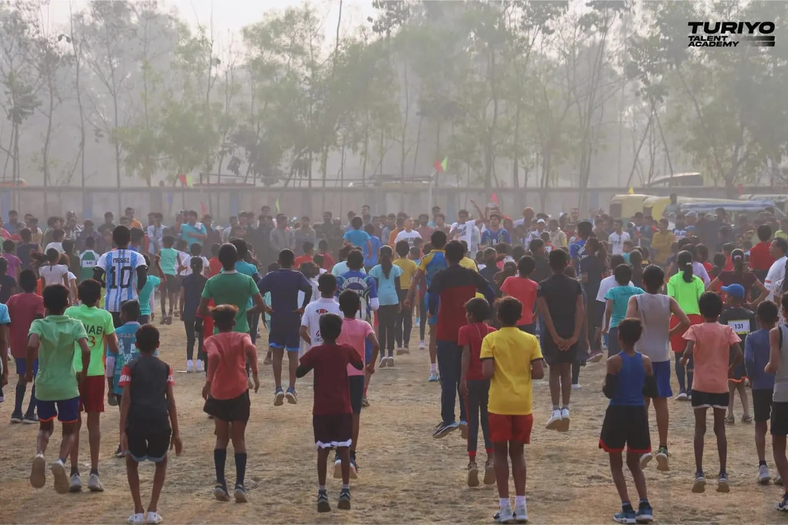 A crowd of young runners jogs towards the start through the morning haze on the school ground