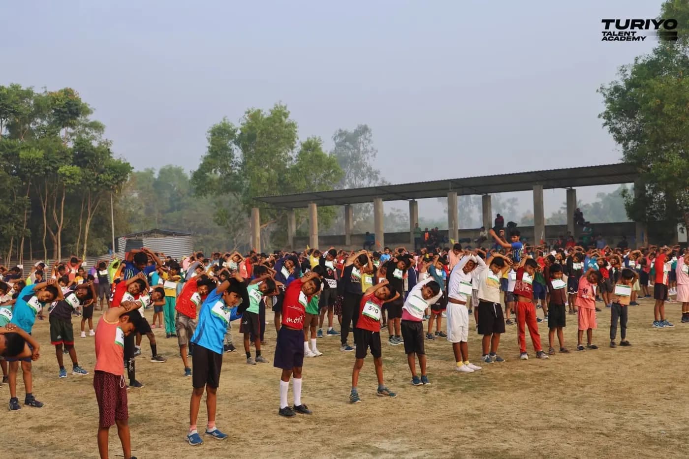Hundreds of children in race bibs stretch together across the Haludbari High School ground in the morning haze