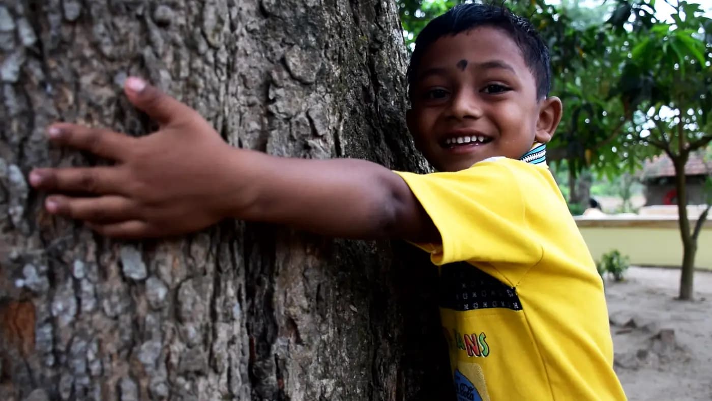 Smiling boy hugging a tree trunk