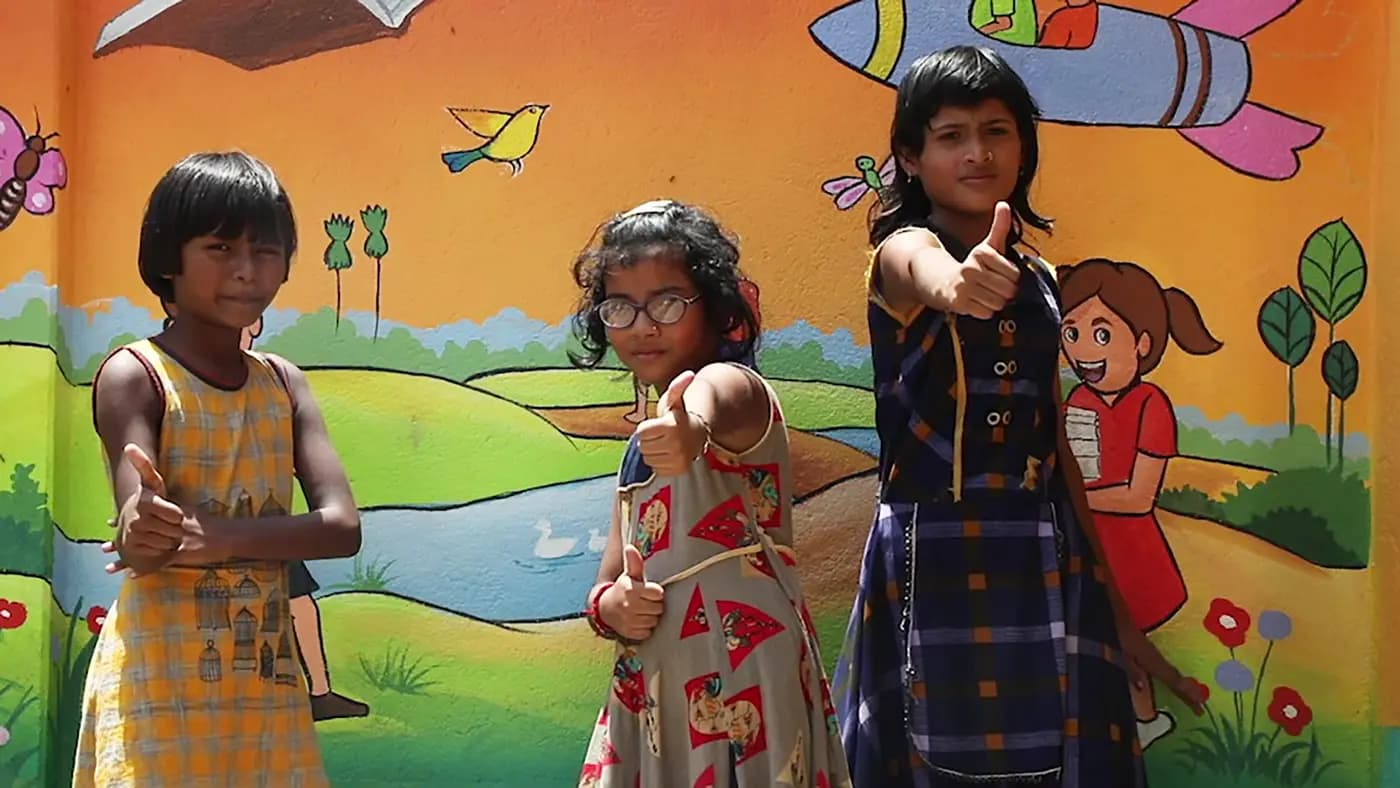 Three girls giving thumbs-up in front of a painted mural