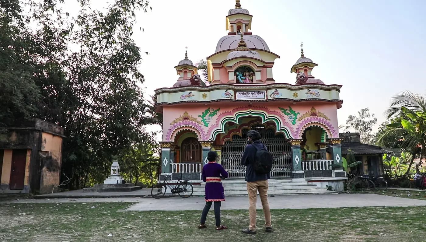 Ornate pink Durga temple in Chauddhachuli with two visitors in front