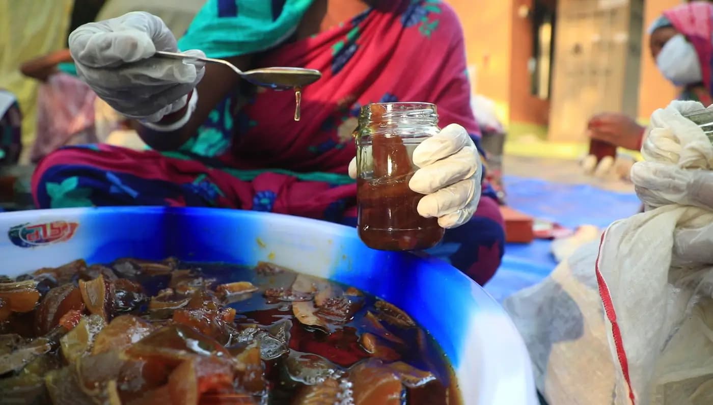 Spooning syrup into a jar over a basin of fruit pickle