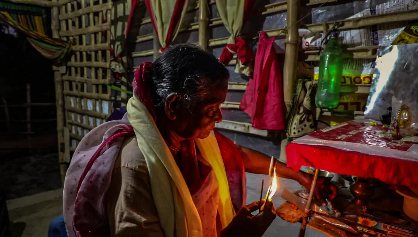 Elderly woman lighting a lamp at her household altar