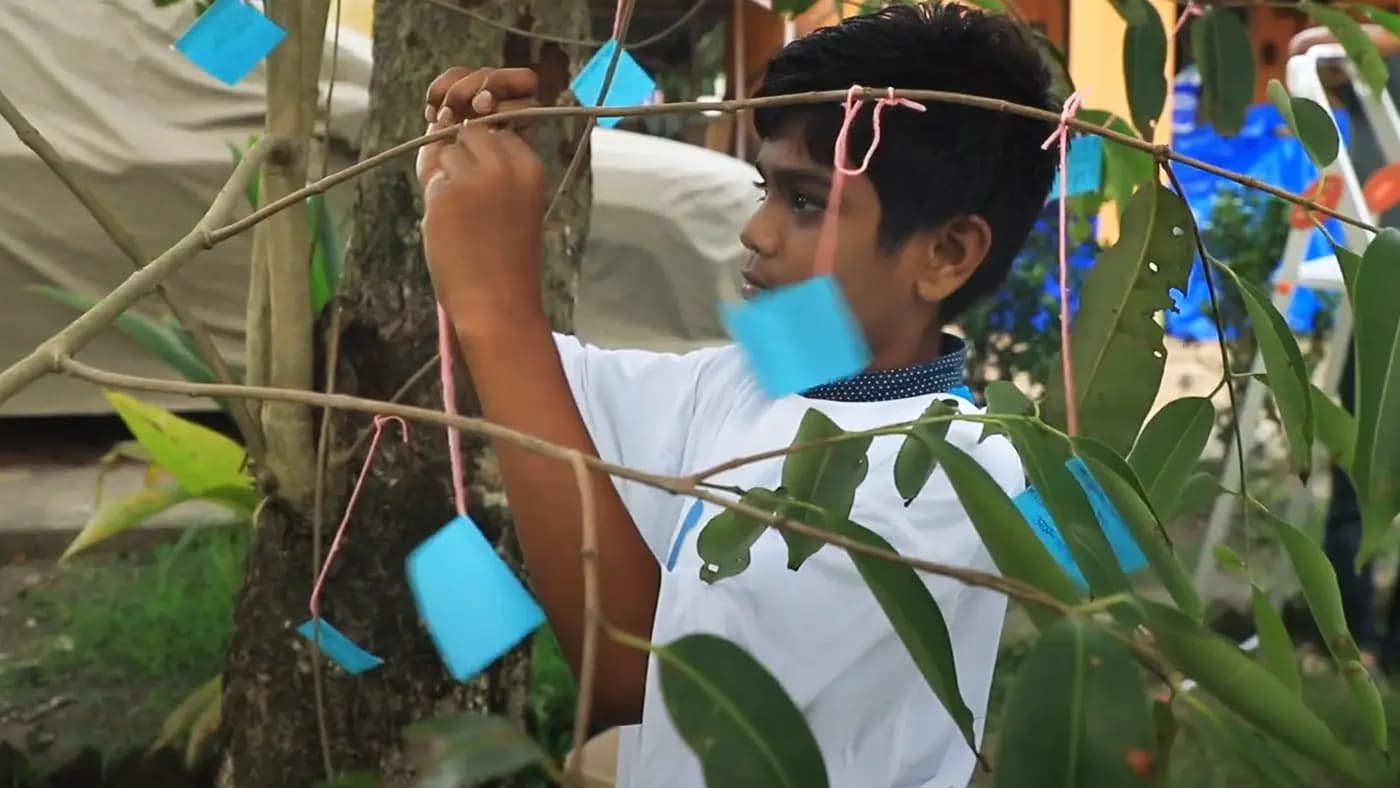 Boy tying paper tags to a tree on World Environment Day