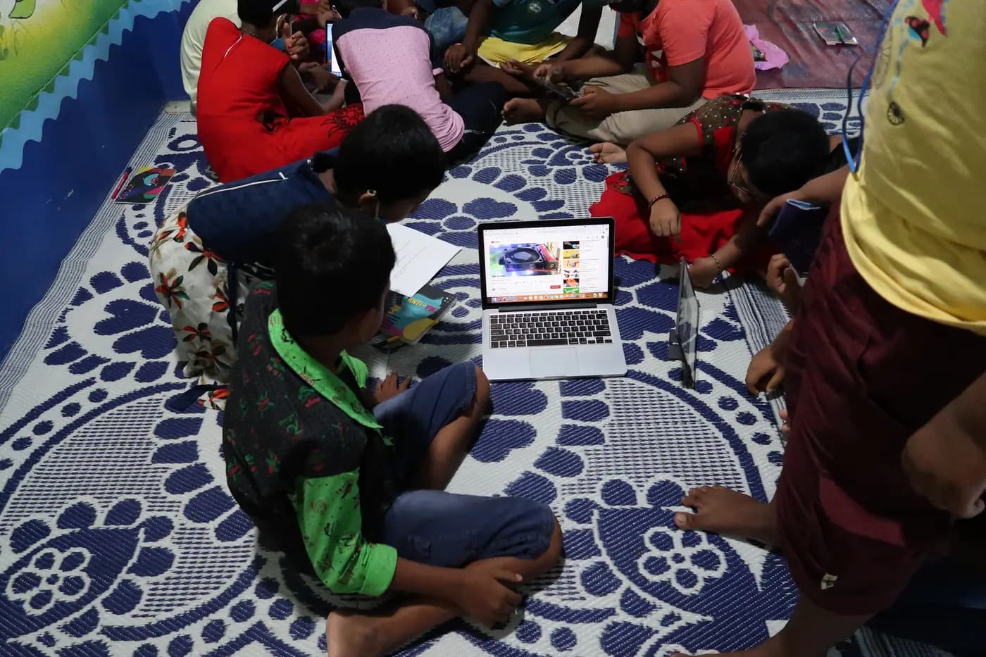 Children gathered around a laptop on a mat