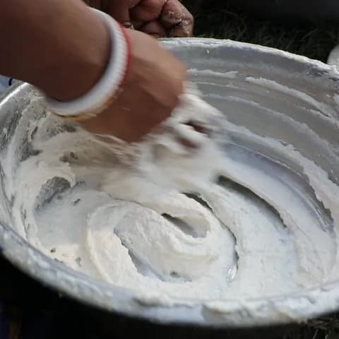 A hand whisking the lentil batter in a steel bowl until it turns light and fluffy