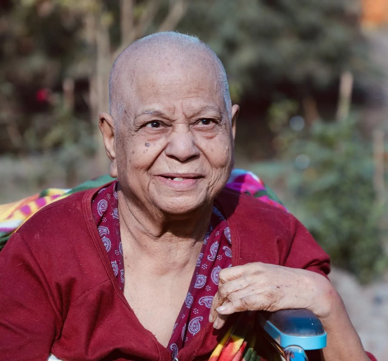 Bandana Maiti, smiling, in a maroon top with a paisley scarf, seated outdoors in winter sun
