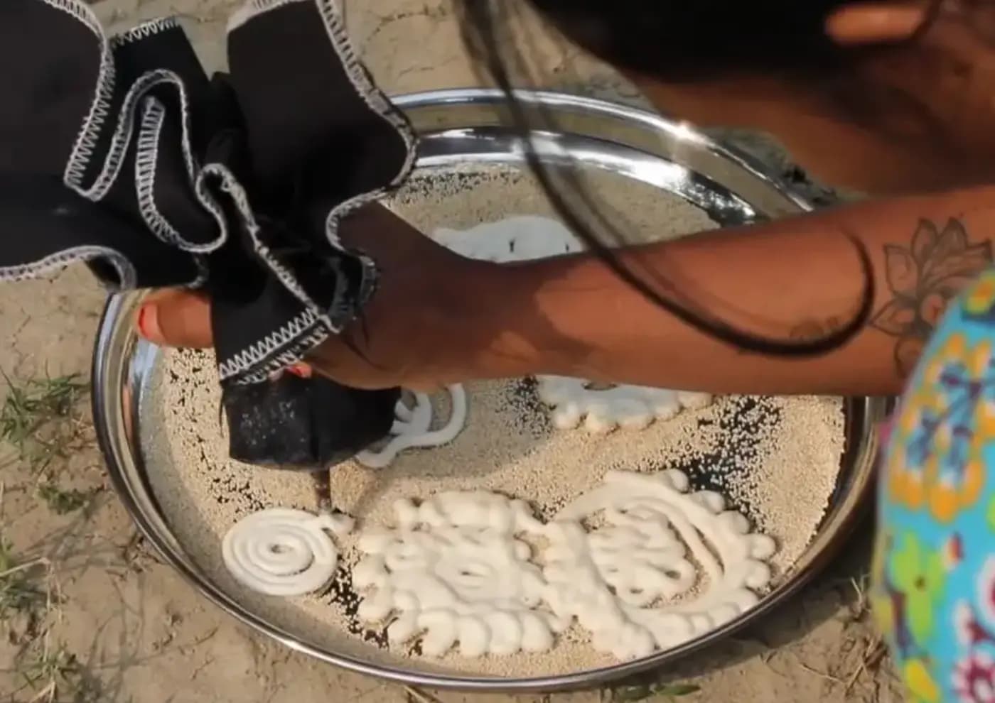 Hands piping lentil paste into ornate gohona bori shapes on a steel plate