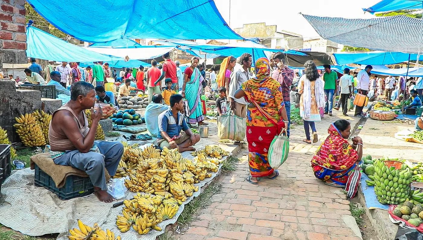 Busy village haat with banana sellers under blue tarpaulins