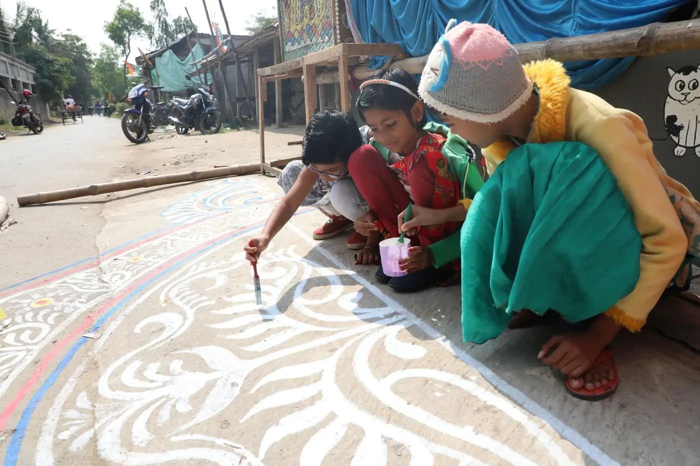 Children painting an alpana design on a village road